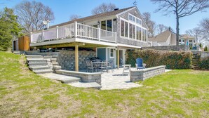 A two-story house with a balcony, stone steps, and a patio area with outdoor furniture. - Patio + Pond View: Serene Cape Cod Escape (Mashpee)