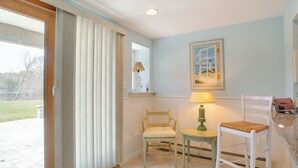 A kitchen with a dining area, a window with curtains, a lamp, and a painting on the wall. - Patio + Pond View: Serene Cape Cod Escape (Mashpee)