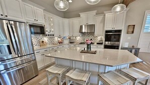 A modern kitchen with white cabinets, stainless steel appliances, and a central island with bar stools. - Rehoboth Beach, Dog Friendly, 5BR, 3 Full Baths, Arbor-Lyn Community, Sleeps 12 (Rehoboth Beach)