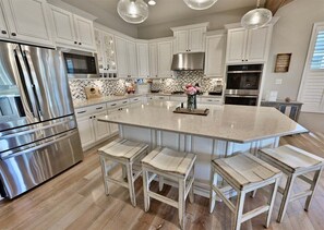 Une cuisine moderne avec des meubles blancs, des appareils en acier inoxydable et un îlot central doté de tabourets de bar.