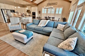 A modern living room with a sectional sofa, a striped armchair, and a dining area with a chandelier.