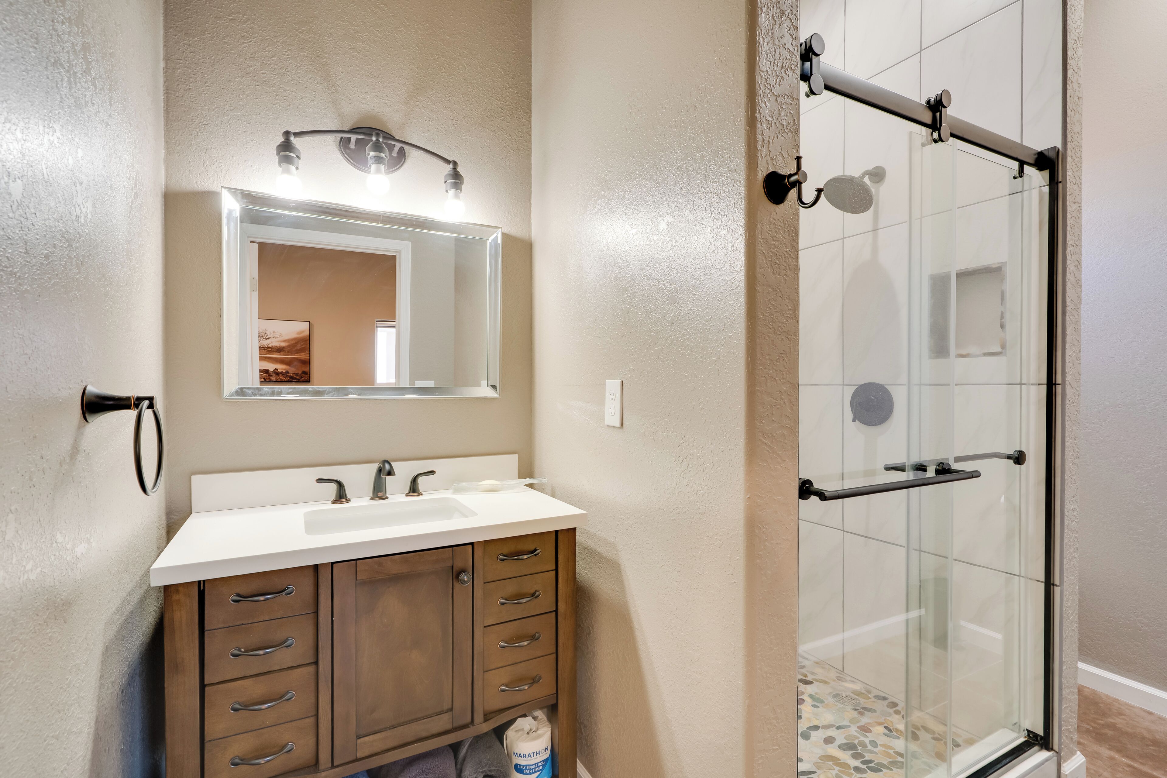 A bathroom with a white sink, wooden vanity, and a glass shower enclosure.