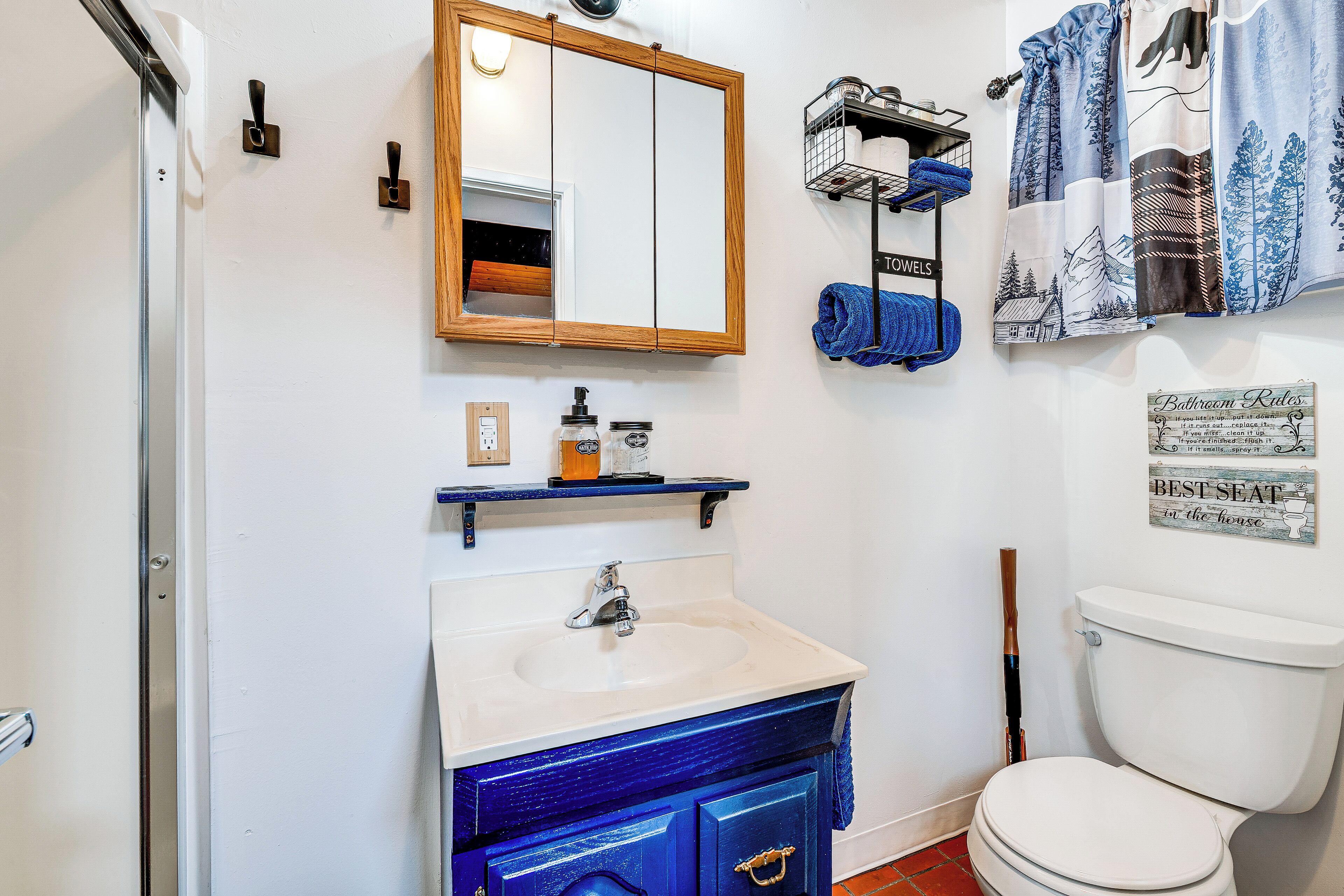 Une salle de bain avec un lavabo blanc, un meuble-lavabo bleu, un miroir à cadre en bois, des toilettes et un porte-serviettes avec des serviettes bleues.