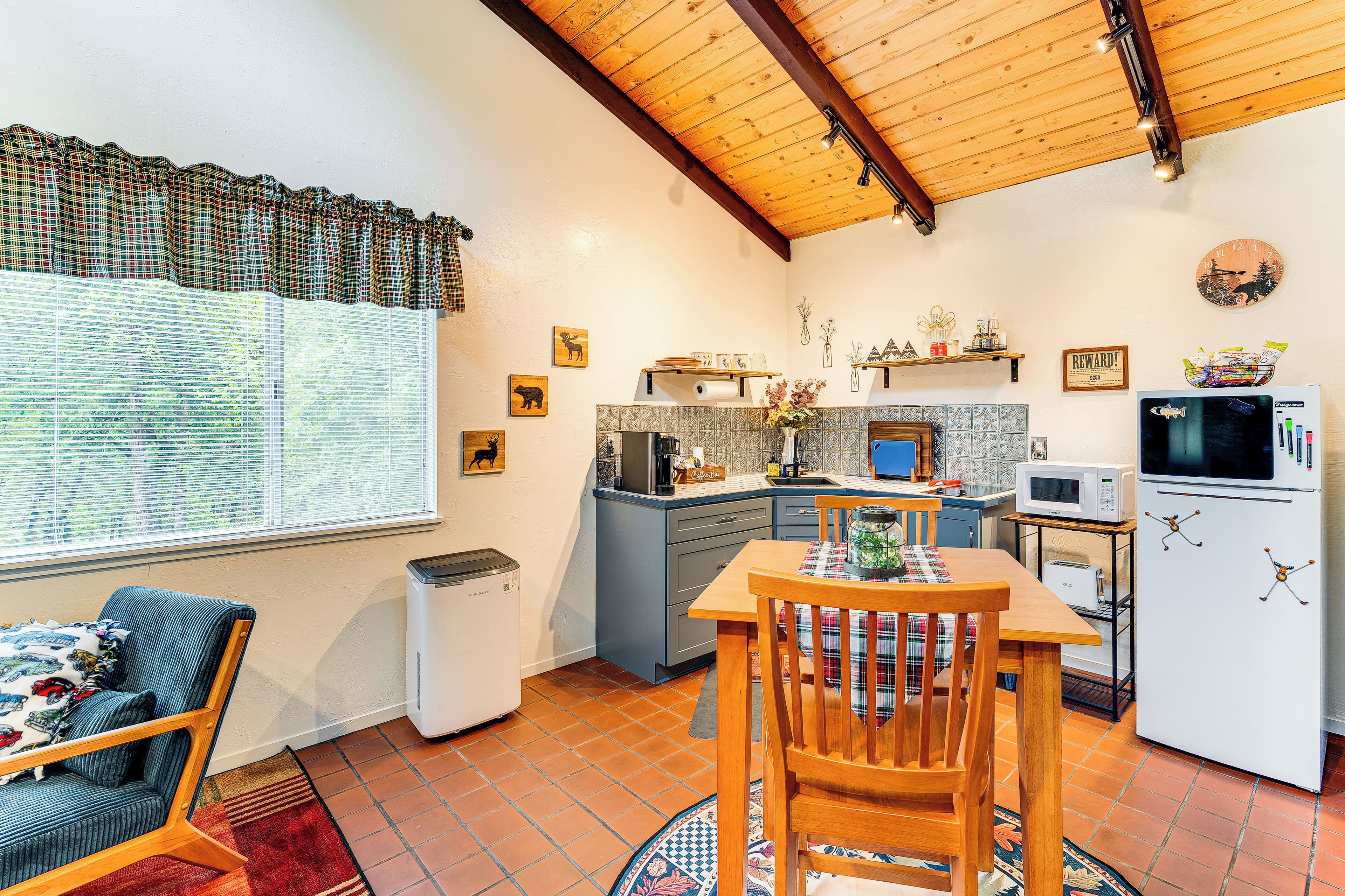 A compact kitchen with a dining area, a window with blinds, a refrigerator, and a microwave.