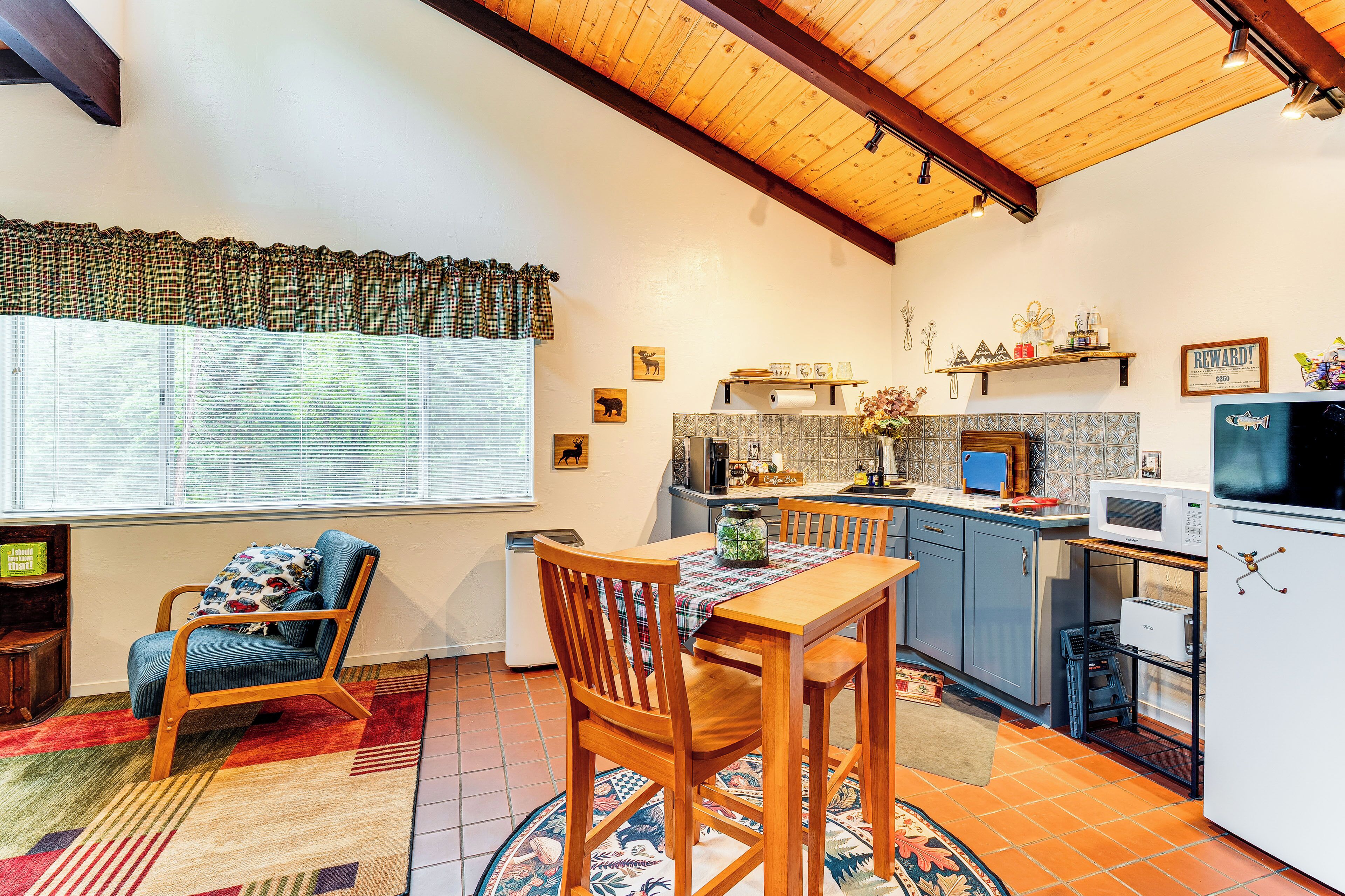A compact kitchen with a dining area, wooden ceiling beams, and a window with blinds.