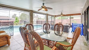 Eine überdachte Terrasse mit Korbmöbeln, einem Glastisch und einem Deckenventilator.