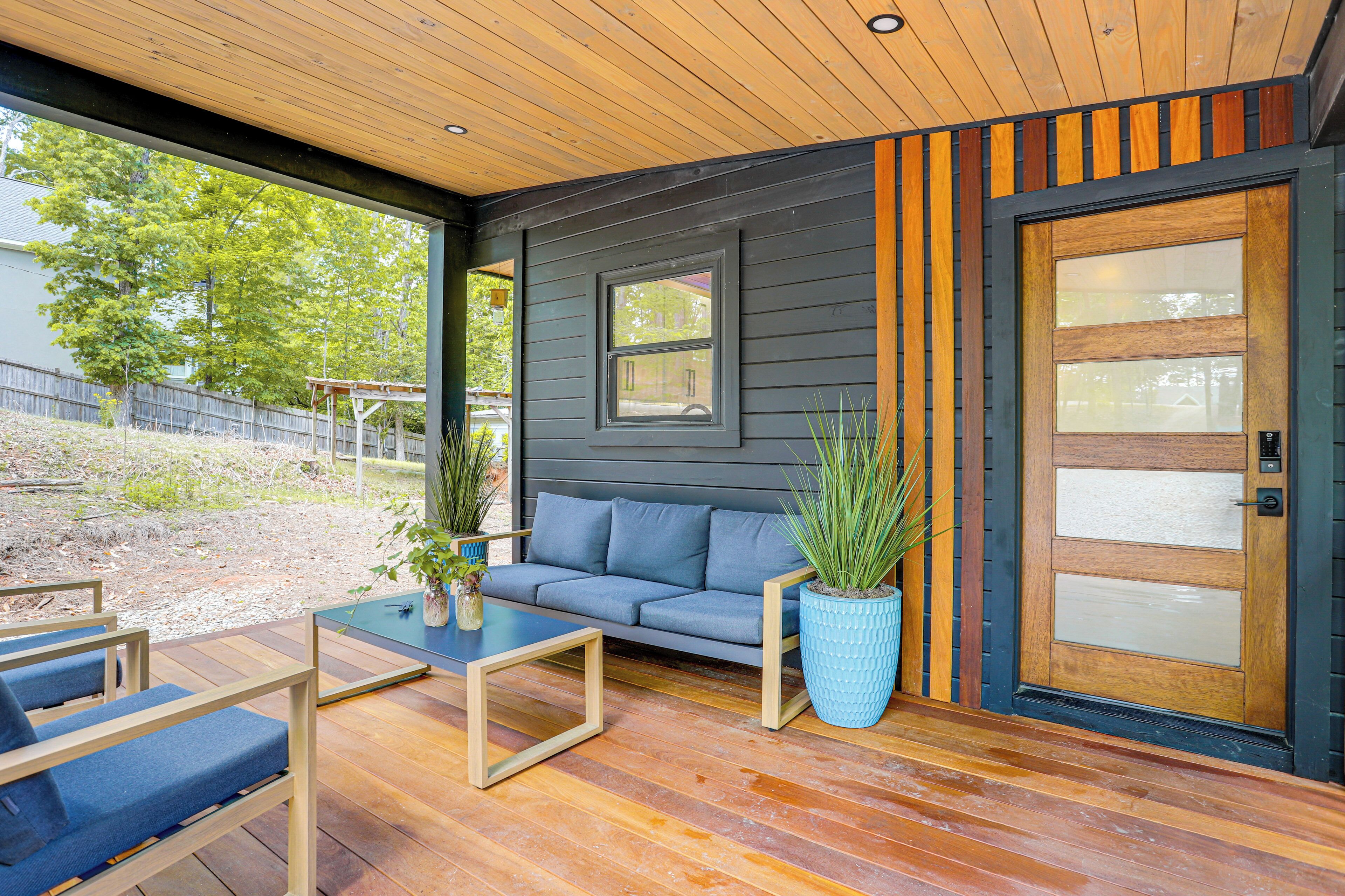 A modern outdoor living space with a wooden deck, a gray sofa, and two blue chairs.
