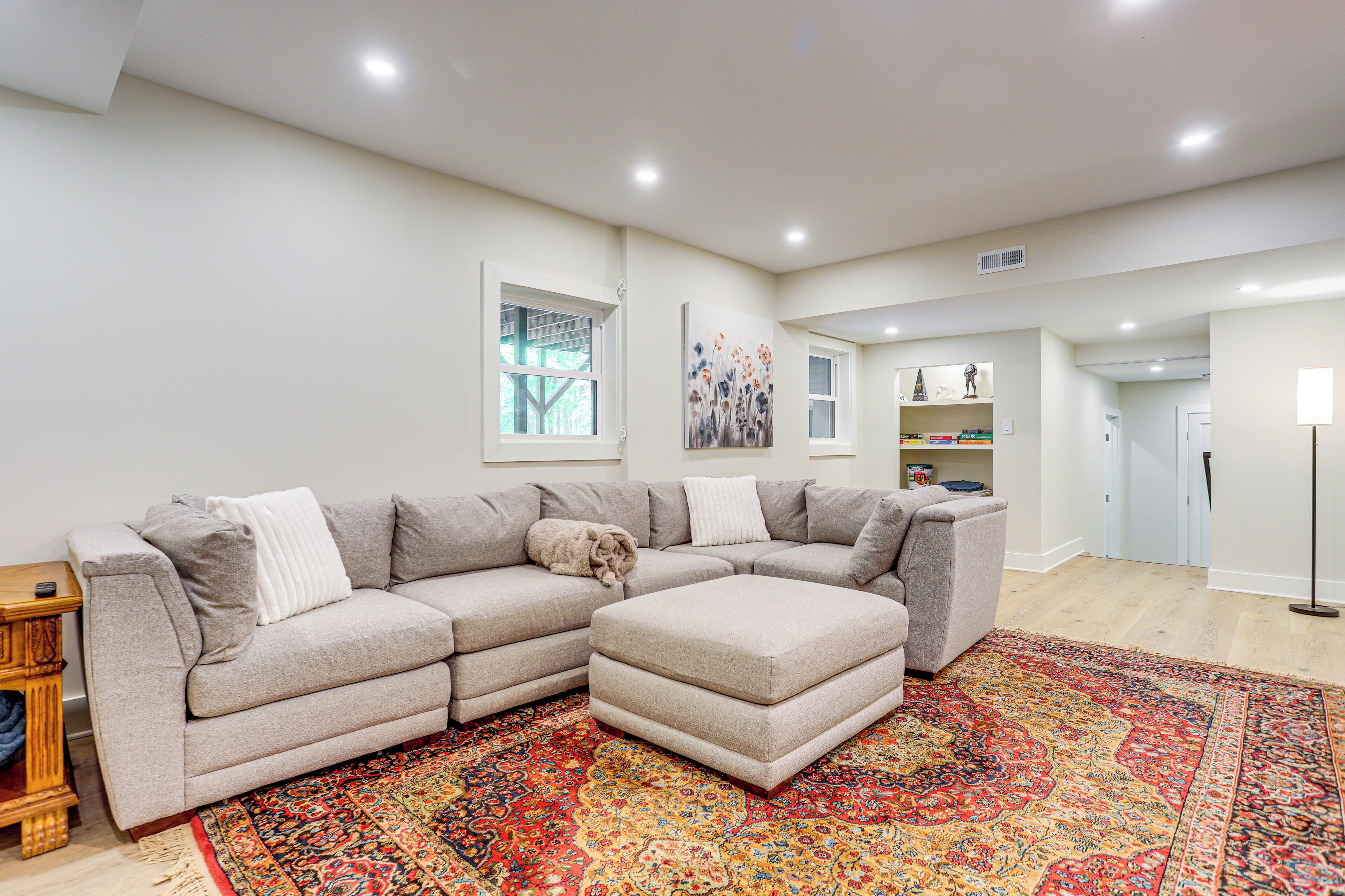 A modern living room with a grey sectional sofa, a matching ottoman, and a vibrant patterned rug.