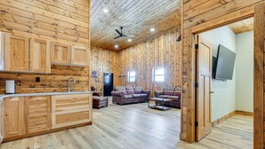 A spacious room with wooden paneling, a kitchen area with wooden cabinets, a sofa, and a television mounted on the wall.