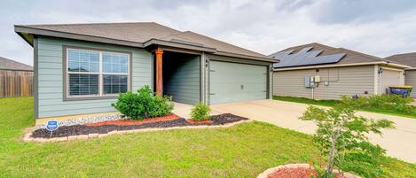 A single-story house with a garage, a small front yard with mulch and plants, and a cloudy sky.