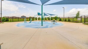 Ein Spielplatz mit einer kreisförmigen, blauen Spielzone, umgeben von einem Zaun und beschattet durch große, blaue Sonnensegel.