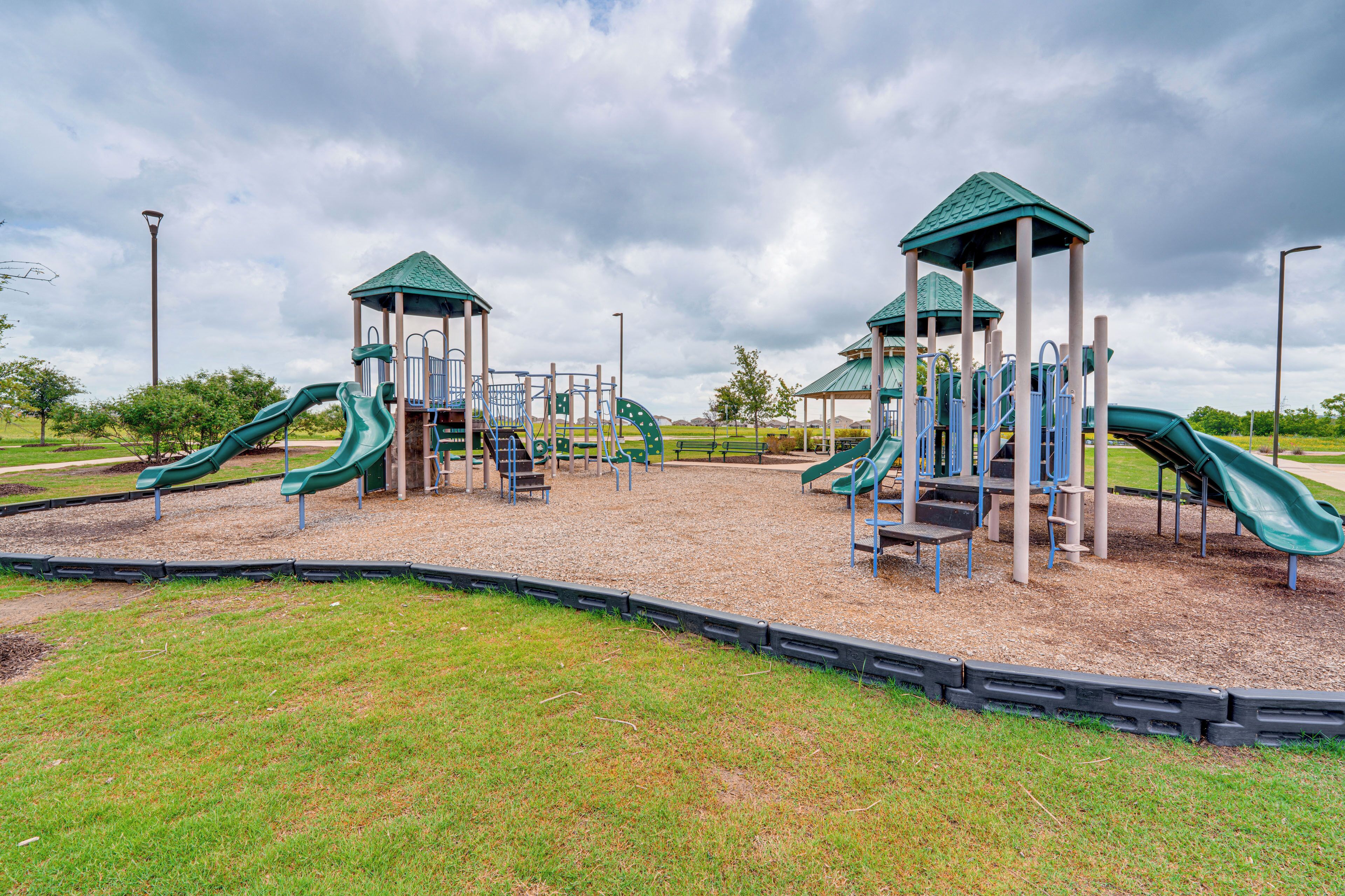 Ein Spielplatz mit mehreren Rutschen und Klettergerüsten, umgeben von einer Rasenfläche und einem bewölkten Himmel.