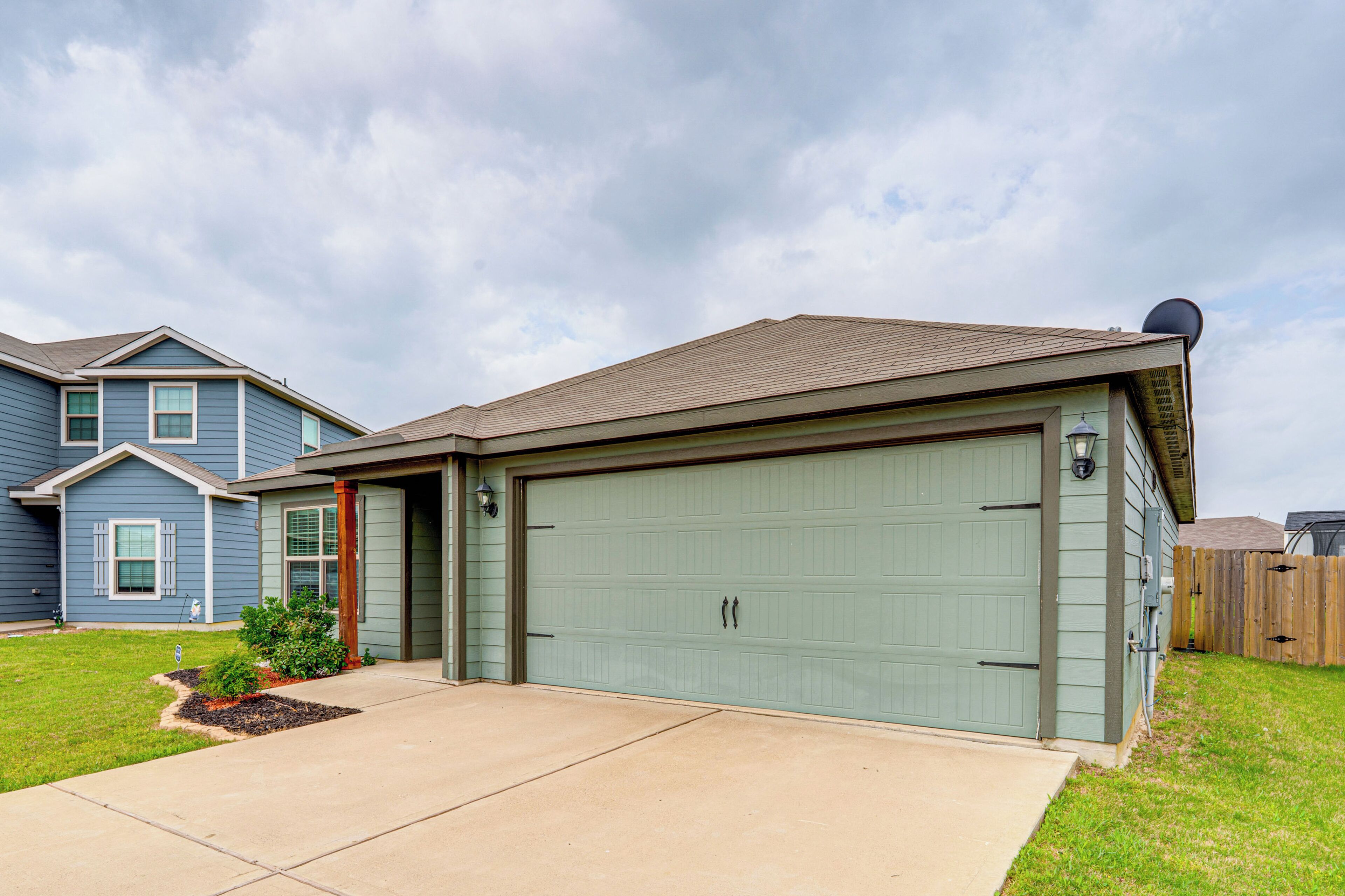 A residential house with a green garage door, a well-maintained lawn, and a clear sky.