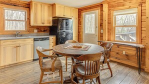 Une cuisine rustique, située dans une cabane en bois, avec une table ronde, des chaises, un réfrigérateur et une fenêtre donnant sur une terrasse.