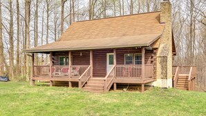 Une cabane en rondins dotée d’une terrasse en bois, d’une cheminée en pierre et d’un porche avec un escalier menant à l’entrée.