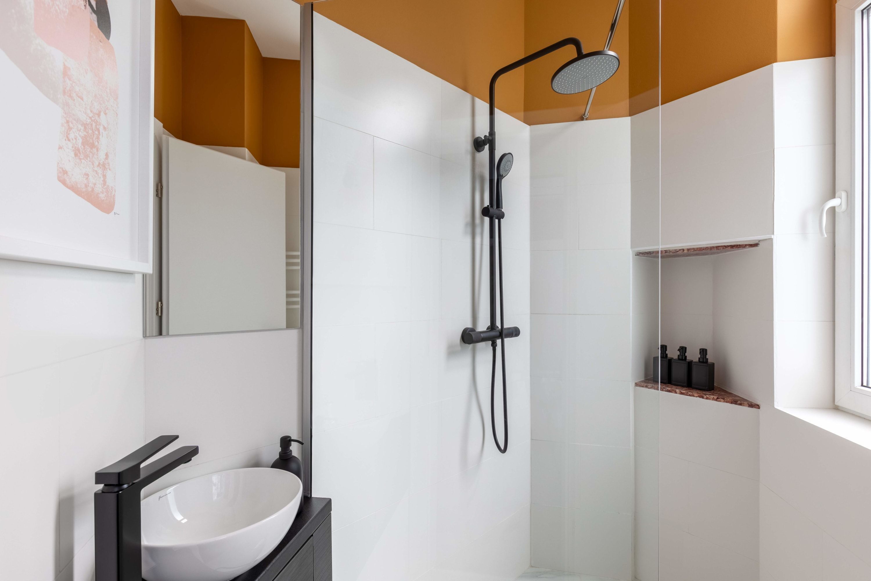 Une salle de bain moderne avec un lavabo blanc, une douche en verre et une fenêtre.