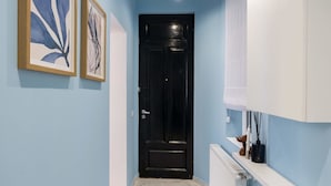 Un pasillo con paredes azul claro, una puerta negra y un piso de mármol blanco. Hay dos cuadros abstractos enmarcados en la pared.