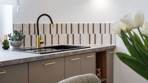 Una cocina moderna con encimera de mármol, tiradores dorados y un lavamanos negro.