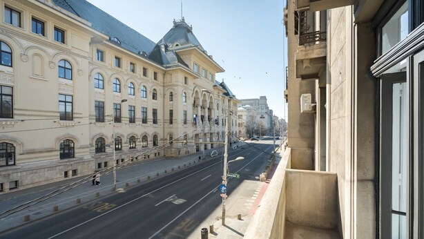 A wide street with a building featuring classical architecture, a clear sky, and a pedestrian walkway. - Elegant 3BR Retreat - Steps Away Cismigiu Gardens (Bucharest)