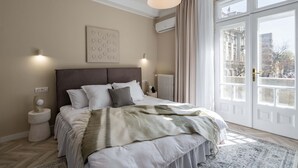 A bedroom with a large bed, a headboard, bedside lamps, a radiator, and a view of the city through large windows. - Elegant 3BR Retreat - Steps Away Cismigiu Gardens (Bucharest)