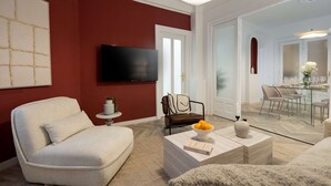 A modern living room with a red accent wall, a flat-screen TV, a comfortable sofa, a coffee table with a bowl of fruit, and a dining area in the background. - Elegant 3BR Retreat - Steps Away Cismigiu Gardens (Bucharest)
