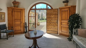 Une pièce avec un meuble en bois, un banc, une table avec un vase, et une vue sur un jardin, visible à travers une porte en arc de cercle.