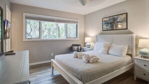 A bedroom with a bed, bedside tables, a window, and a ceiling fan. - Kiawah Exclusives | 165 Marsh Hawk Lane (Kiawah Island)