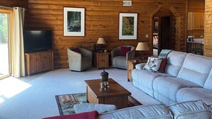 A cozy cabin interior with a wooden ceiling, a large sofa, a television, and framed pictures on the walls. - Towering Pines Lodge: A Hidden Haven 10 Miles from Wisconsin Dells (Wisconsin Dells)