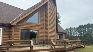 A log cabin with a deck, outdoor seating, and a large window. - Towering Pines Lodge: A Hidden Haven 10 Miles from Wisconsin Dells (Wisconsin Dells)