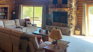 A cozy log cabin interior with a stone fireplace, wooden ceiling, and a large sofa. - Towering Pines Lodge: A Hidden Haven 10 Miles from Wisconsin Dells (Wisconsin Dells)