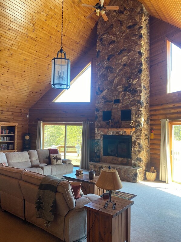 A cozy log cabin interior with a stone fireplace, wooden ceiling, and a large sofa. - Towering Pines Lodge: A Hidden Haven 10 Miles from Wisconsin Dells (Wisconsin Dells)