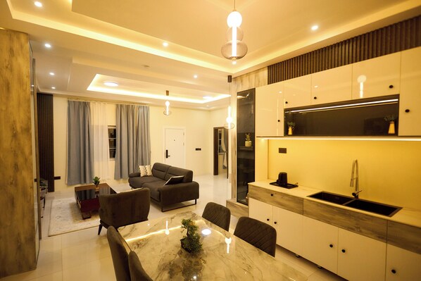 A modern living room with a sofa, dining table, and kitchen area with a sink and cabinets. - Abram Hills Hotel Ltd (Koforidua)