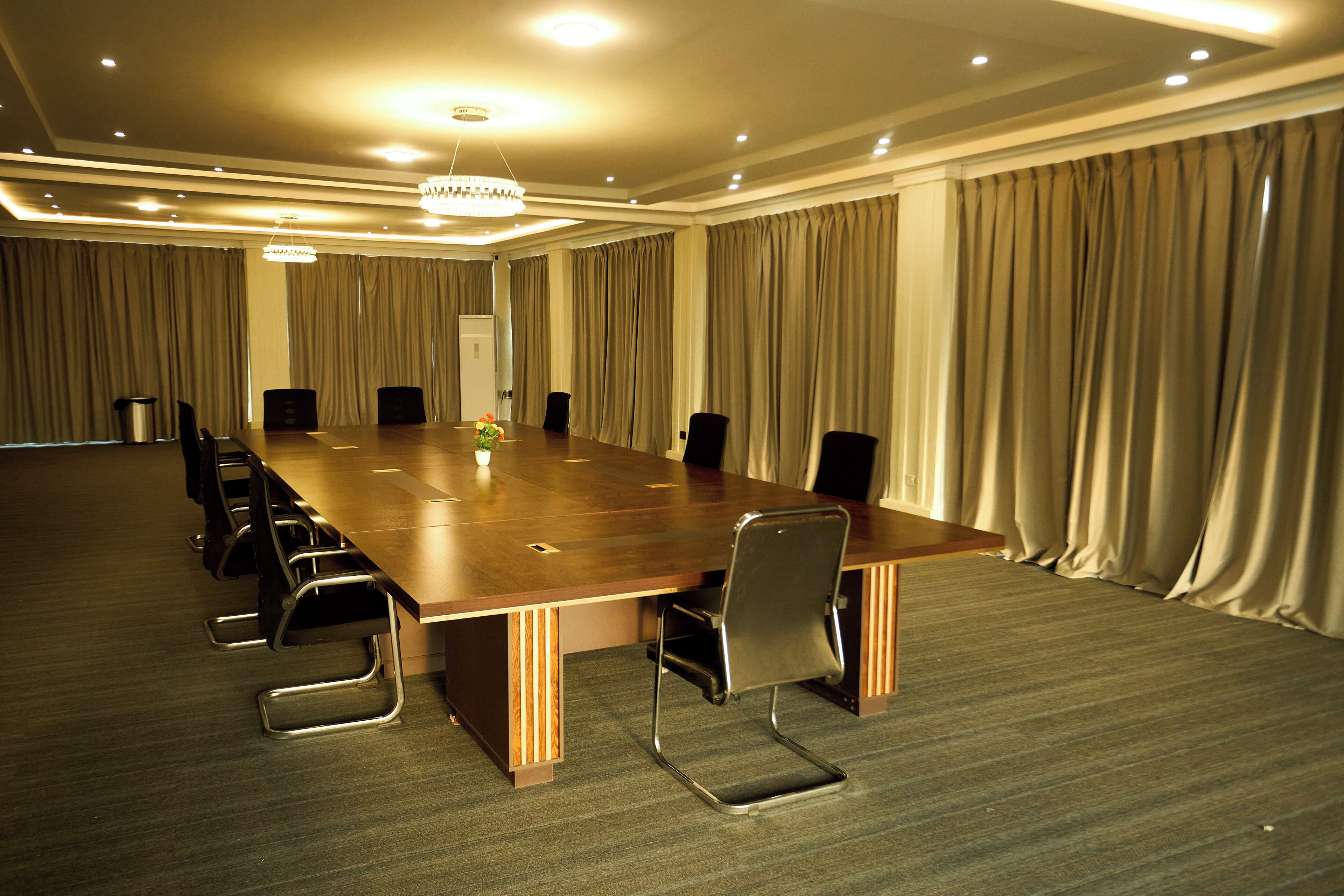Une salle de conférence avec une longue table, des chaises, un lustre et des rideaux.