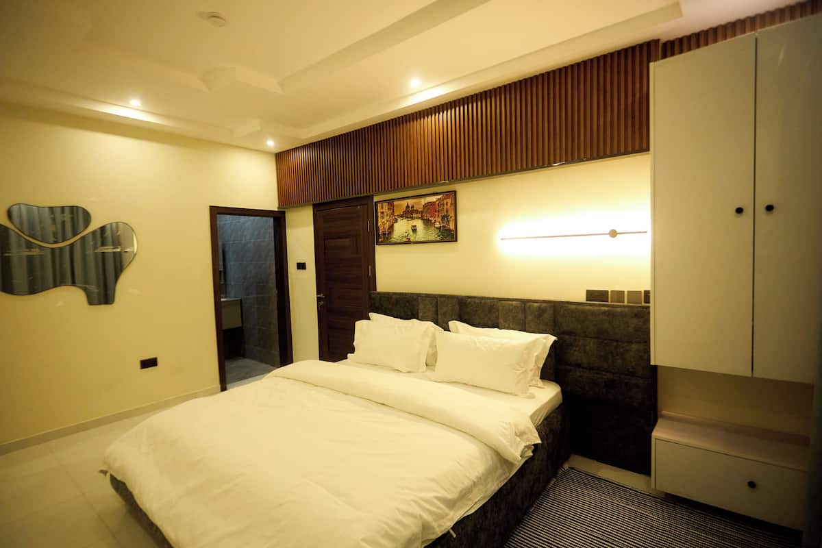 A bedroom with a bed, a headboard, a wardrobe, a painting, and a mirror.
