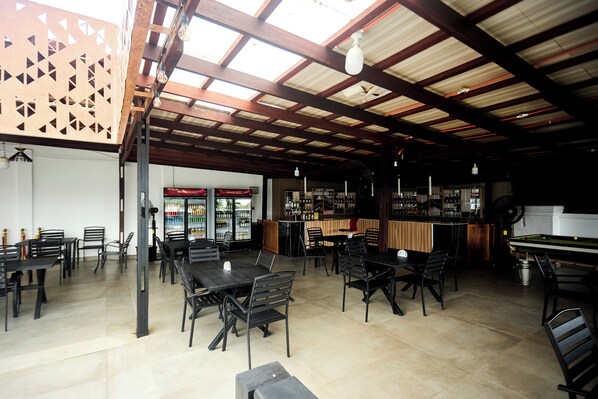 An indoor dining area with multiple tables and chairs, a bar area with a counter and shelves, and a ceiling with exposed beams and lighting fixtures. - Abram Hills Hotel Ltd (Koforidua)