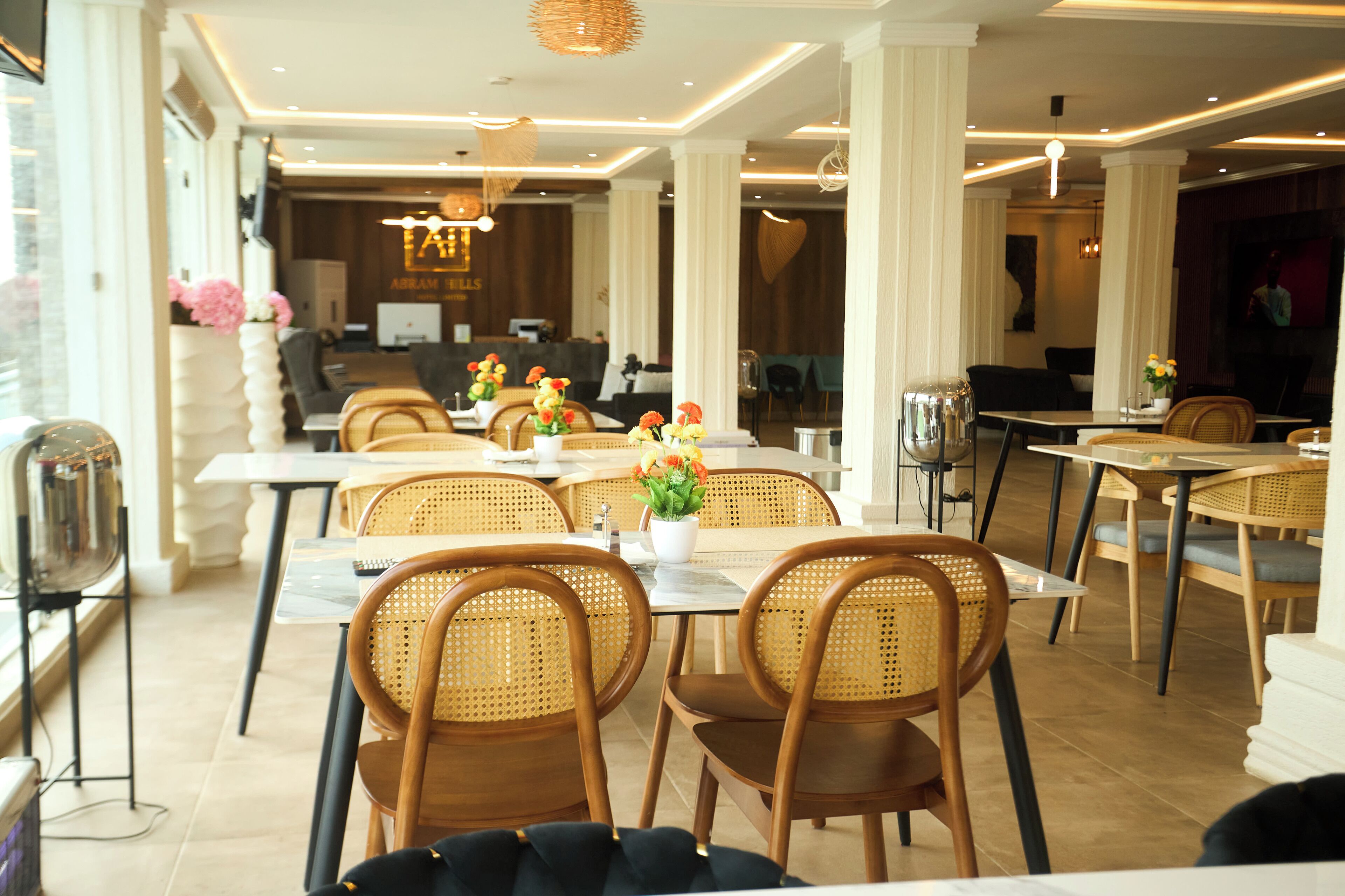 Un espace de restauration moderne avec des chaises en osier, une table centrale décorée de fleurs et, au fond, un comptoir d'accueil.