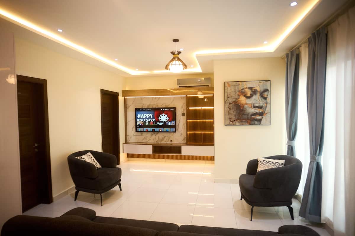 A modern living room with a flat-screen TV, two armchairs, and a sofa.
