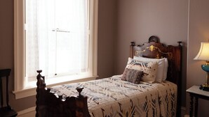 A bedroom with a large window, a wooden bed with patterned bedding, and a bedside table with a lamp. - Bat Masterson - Historic Hotel Room (Cimarron)