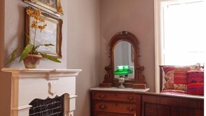 A room with a fireplace, a mirror, a dresser, and a window. - Bat Masterson - Historic Hotel Room (Cimarron)