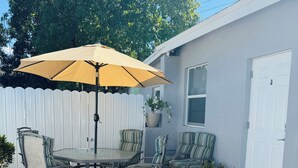 An outdoor patio with a round table and chairs, a large umbrella, and potted plants.