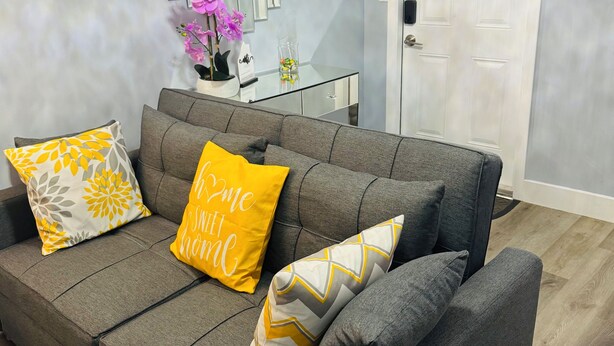 A grey sectional sofa with three cushions, a glass coffee table, and a decorative mirror with vertical panels.
