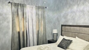 A bedroom with a bed, curtains, a nightstand, a lamp, and a ceiling fan.