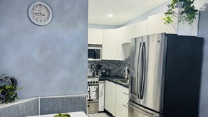 A modern kitchen with stainless steel appliances, a white table with a green bowl, and a clock on the wall.