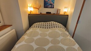 Ein Schlafzimmer mit einem Bett, das eine gebogene Bettdecke, zwei Nachttischlampen, einen Nachttisch mit einer Vase und ein Bild an der Wand hat.