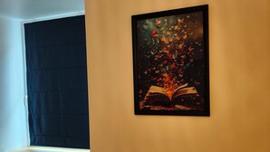Ein gemütliches Wohnzimmer mit einem großen Fenster, einer Couch und einem Wandbild, das ein offenes Buch mit Herbstlaub zeigt.