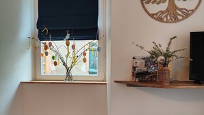 Ein Zimmer mit Fenster, einer Wanddekoration mit Baummotiv, einem Regal mit einer Vase und einem gefliesten Boden.