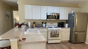 A modern kitchen with white cabinets, a stainless steel refrigerator, a microwave, a stove, and a sink.