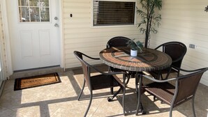 A covered patio with a round table and four chairs, a potted plant, and a door with a window.