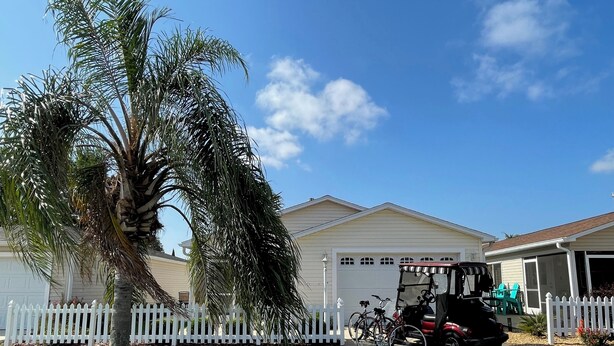 A residential area with a white picket fence, a palm tree, and a garage door.