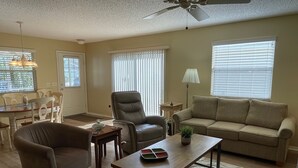 A living room with a sofa, armchairs, a coffee table, and a ceiling fan.